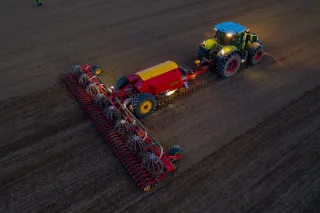 Traktor táhne secí stroj Väderstad Inspire po poli za soumraku.